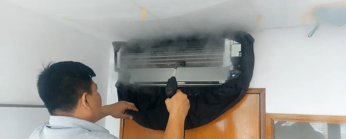 Kim's Aircon technician steam-cleaning an open wall-mounted air conditioner in Singapore, with visible steam and a catchment bag fitted